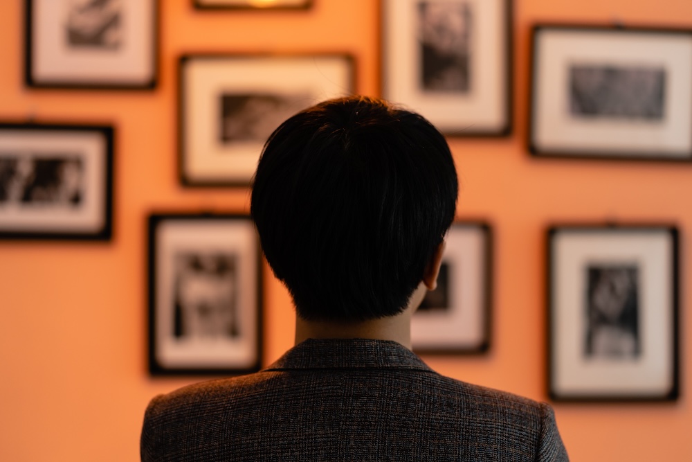 back of person's head as they stand looking at a wall of photos in a museum or gallery